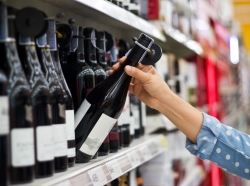 A hand reaching for a bottle of wine on a store shelf. Photo by ipopba / Getty Images