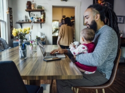 Dad feeding baby while working from home on laptop computer at dining room table, photo by Inti St. Clair/Adobe Stock