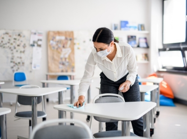 Teacher back at school after COVID-19 lockdown, disinfecting desks, photo by Halfpoint/AdobeStock