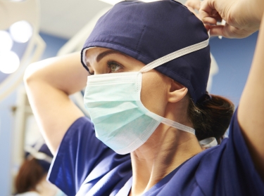 Young female surgeon putting on her mask, photo by Anna Bizon/Adobe Stock