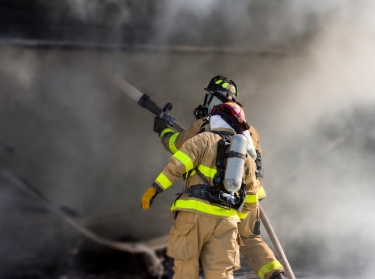 Two firefighters holding a hose and surrounded by smoke