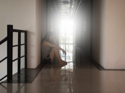 A woman sitting alone in a corridor resting her head in her hand