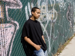 black teen standing by fence covered in graffiti