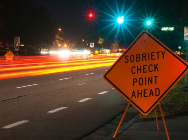 Sobriety checkpoint sign on the side of a busy highway at night