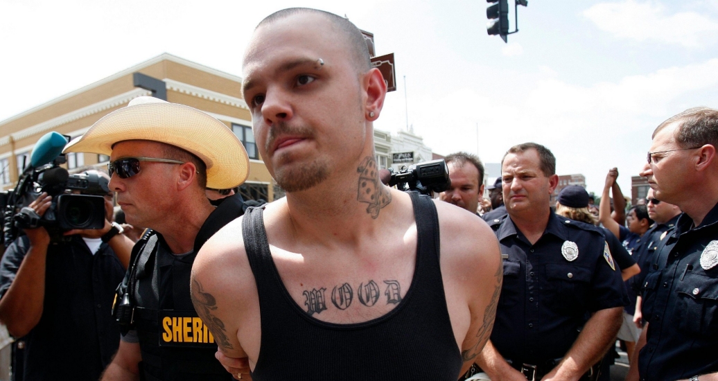 A white supremacist protester is escorted away in handcuffs by a sheriff during a demonstration in Paris, Texas, July 21, 2009