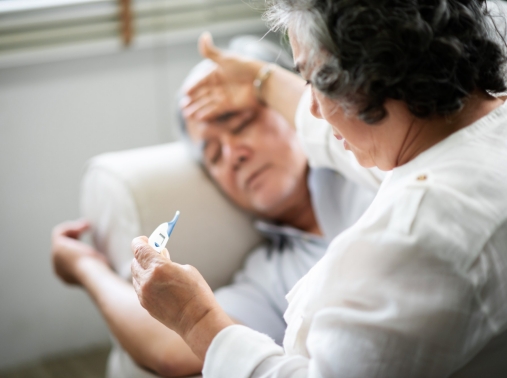 A sick man lying on a couch while his wife reads a thermometer