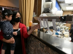 Owner Jan-Ie Low holds her nephew as she moves order tickets at Satay Thai Bistro and Bar in Las Vegas, Nevada, March 28, 2021, photo by Bridget Bennett/Reuters