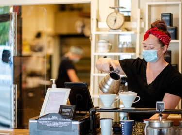 A barista making coffee while wearing a mask, photo by stockstudioX/Getty Images