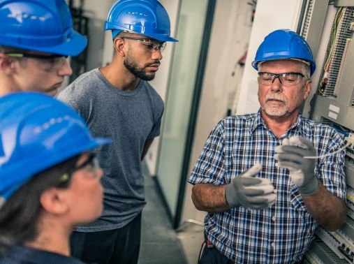 Electrician teaching his apprentices how to strip the wires in the distribution board