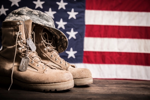 A soldier's hat, boots, and dog tags in front of an American flag