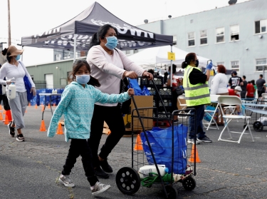 A family pushes a cart after receiving groceries during a Mother's Day food distribution event organized, Los Angeles, California, May 9, 2020, photo by Patrick T. Fallon/Reuters