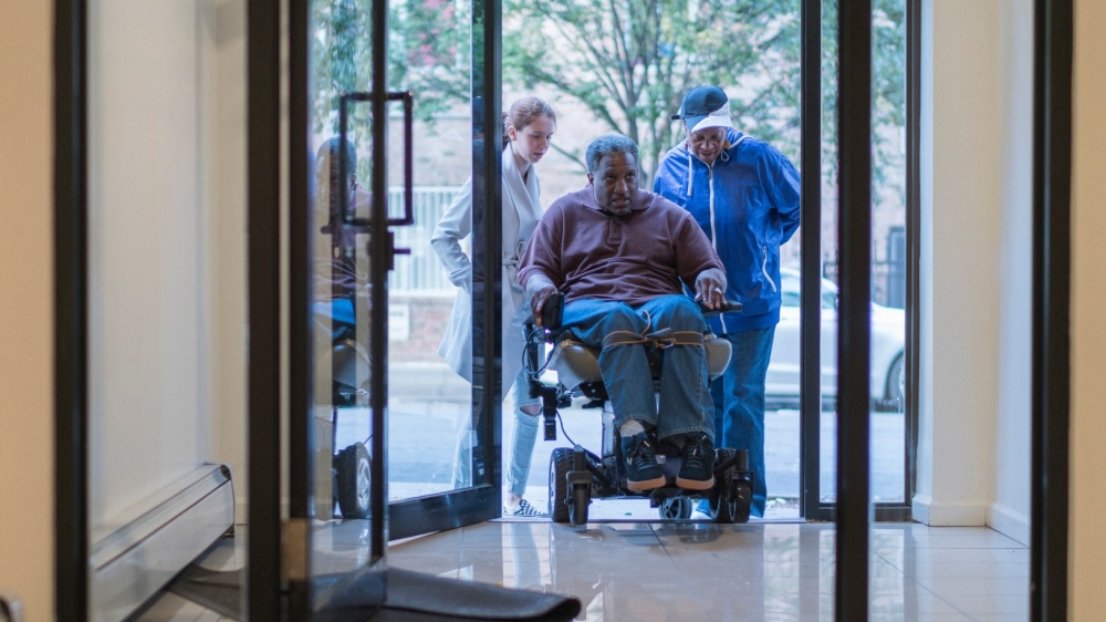 A teenage girl and woman helping a disabled man through the door