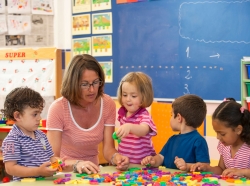 Female teacher with preschool boys and girls learning alphabet in classroom