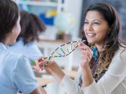 A school teacher talks with a student, holding a DNA helix model, photo by Steve Debenport/Getty Images