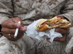 An individual in the fatigues worn by U.S. Marines holding a cigarette and hamburger