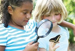 Two girls look at a butterfly through a magnifying glass.