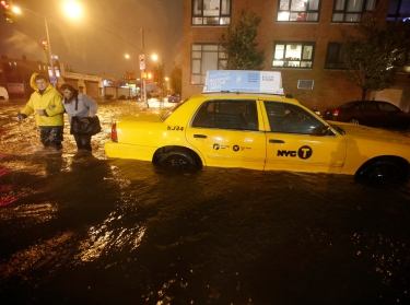Pedestrians walk past a submerged taxi in Brooklyn, New York, during Hurricane Sandy last year.