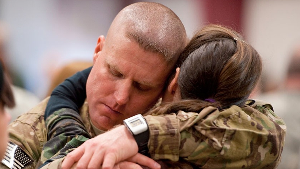 The face of a soldier as he hugs a woman.