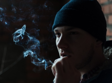 A young man in a cap smokes a cigarette
