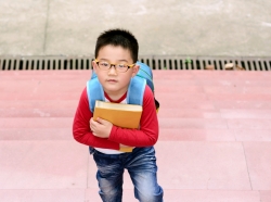 A boy with a blue backpack holds a book