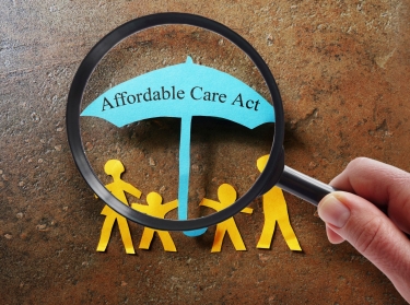 Paper family under a Affordable Care Act umbrella with magnifying glass