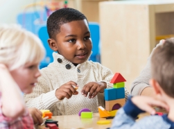 A boy in preschool playing with building blocks with classmates