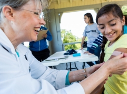 Older female nurse applying a bandaid to young girl at a community clinic