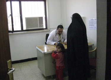 A doctor sits behind a desk while speaking to a woman and her young child