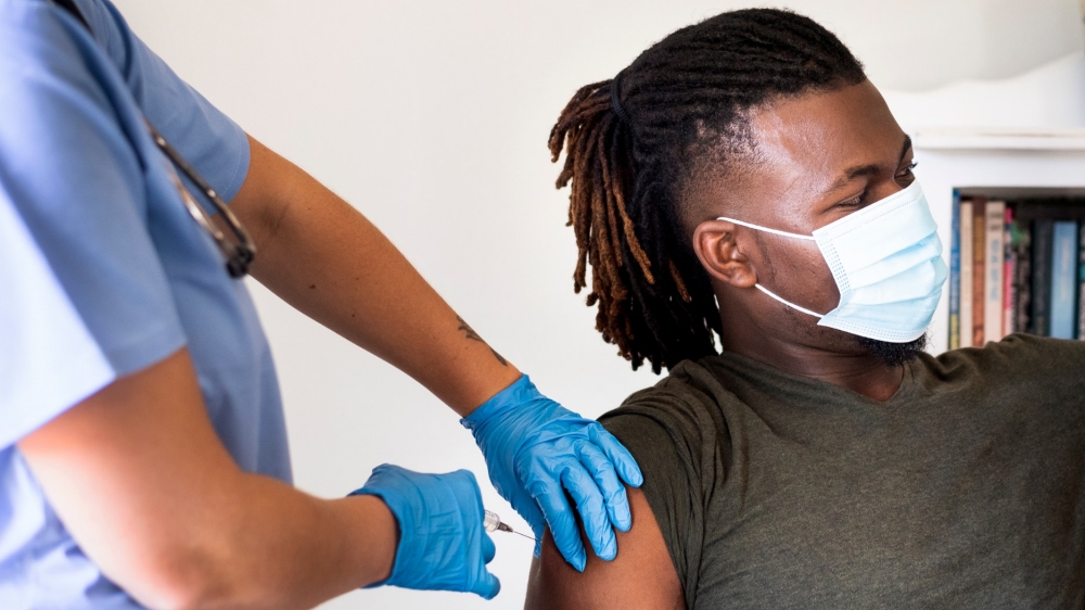 Healthcare worker wearing a protective face mask giving a vaccine injection to a young man in a clinic