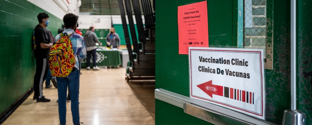 Signs on a door to a school gym point students to wait in line to receive COVID-19 vaccinations