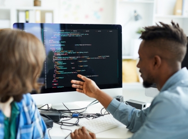 Busy young interracial colleagues analyzing computer code on computer: African man pointing at monitor and asking coworker in office, photo by pressmaster/Adobe Stock