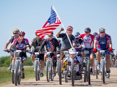 Group of adults riding bikes together with an American flag attached to the front bike