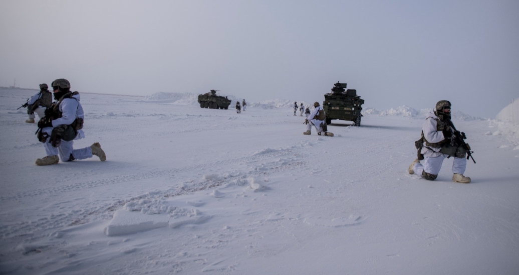 U.S. soldiers kneel on the ground in an open, snowy landscape keeping watch