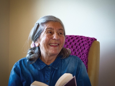 A senior woman smiling and holding a book, photo by the Weinberg Center