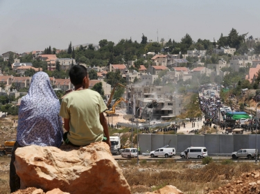 Palestinians watch Israeli heavy machinery demolishing vacant apartment blocs by order of Israel's high court, in the West Bank Jewish settlement of Beit El near Ramallah July 29, 2015