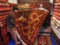Afghan carpet salesmen fold a carpet after showing it to customers at a shop in Kabul