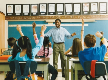 Teacher standing in front of a classroom of students with hands raised