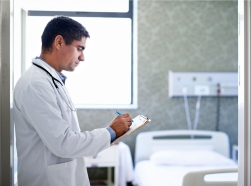 Doctor filling out a patient's chart in front of an empty hospital room