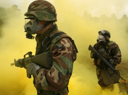 Sailors patrol through yellow smoke simulating chemical, biological, and radiological exposure during combat