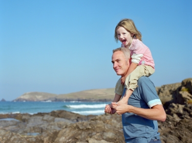 Father carrying daughter on his shoulders by the sea in Cornwall, England