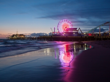 The Santa Monica Pier in California, illuminated at night with a reflection on shoreline