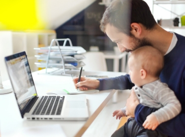 Dad works from home, holding baby on his lap