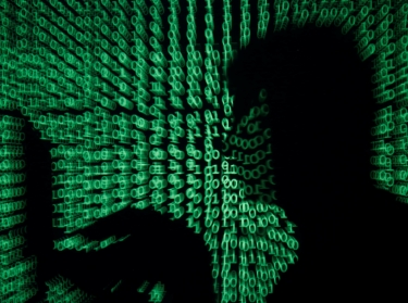 A man holds a laptop computer as cyber code is projected on him
