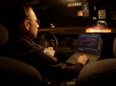 A male police officer working on a laptop while sitting in a vehicle