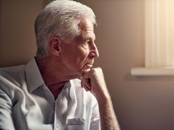 Elderly man with chin on his fist, looking out a sunny window