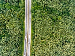 Aerial view of a highway with cars and trucks in the middle of a green forest