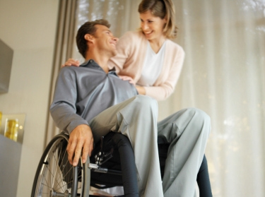 a man sitting in a wheelchair with his partner or wife at his shoulder