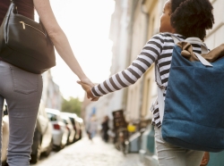 Seen from behind, a woman holding hands with her daughter on a city sidewalk