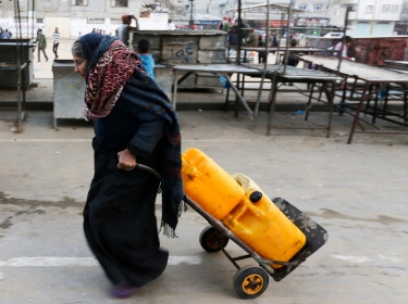 A Palestinian woman drags a cart loaded with water containers after filling them from a public tap in the city of Rafah in the southern Gaza Strip, February 28, 2017