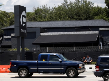 Police officials stand on the sidewalk as cars drive on the road in front of the Pulse night club, following a shooting in Orlando, Florida, June 21, 2016